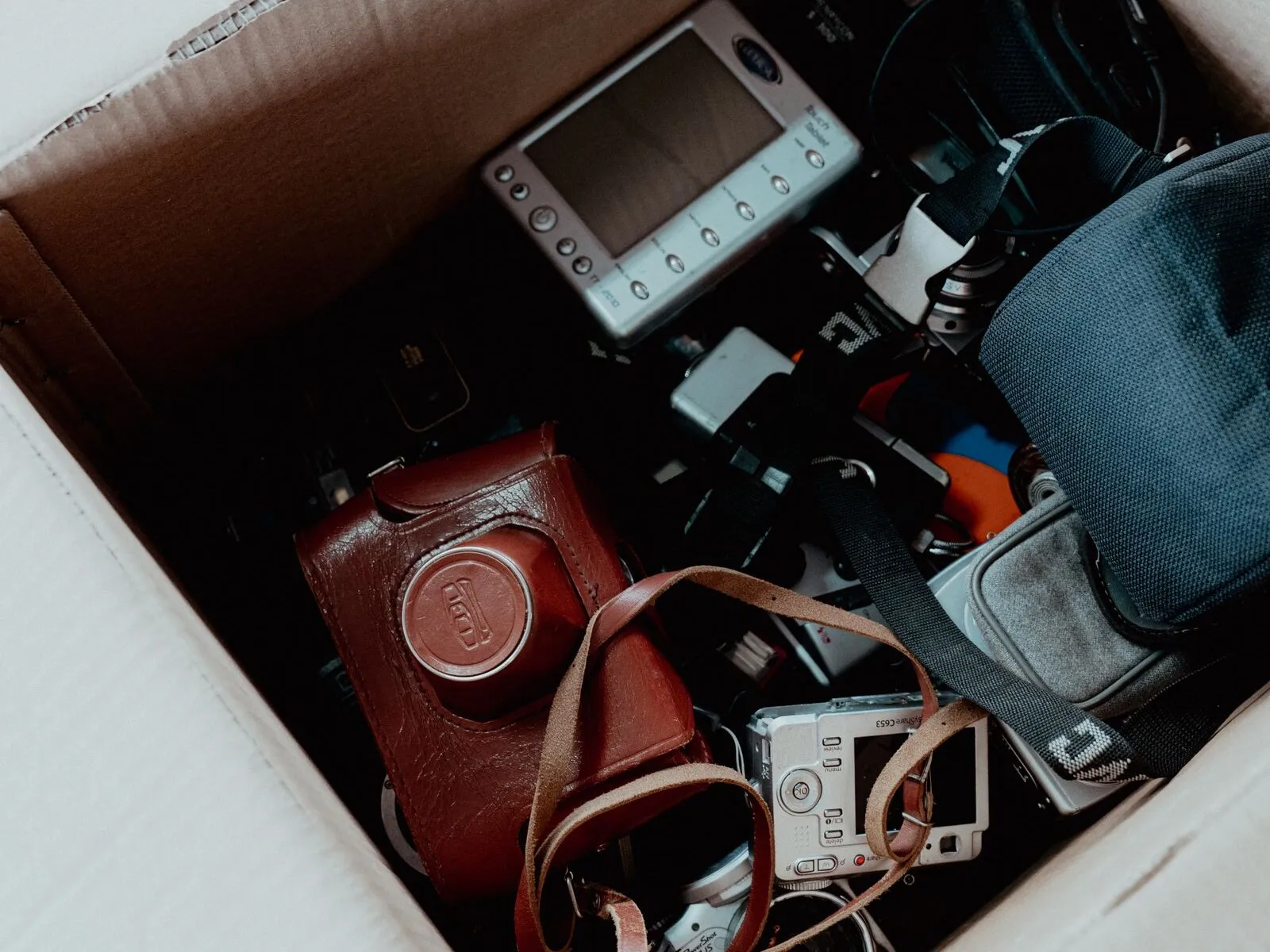An open cardboard box packed with cameras, a PDA and a camera bag