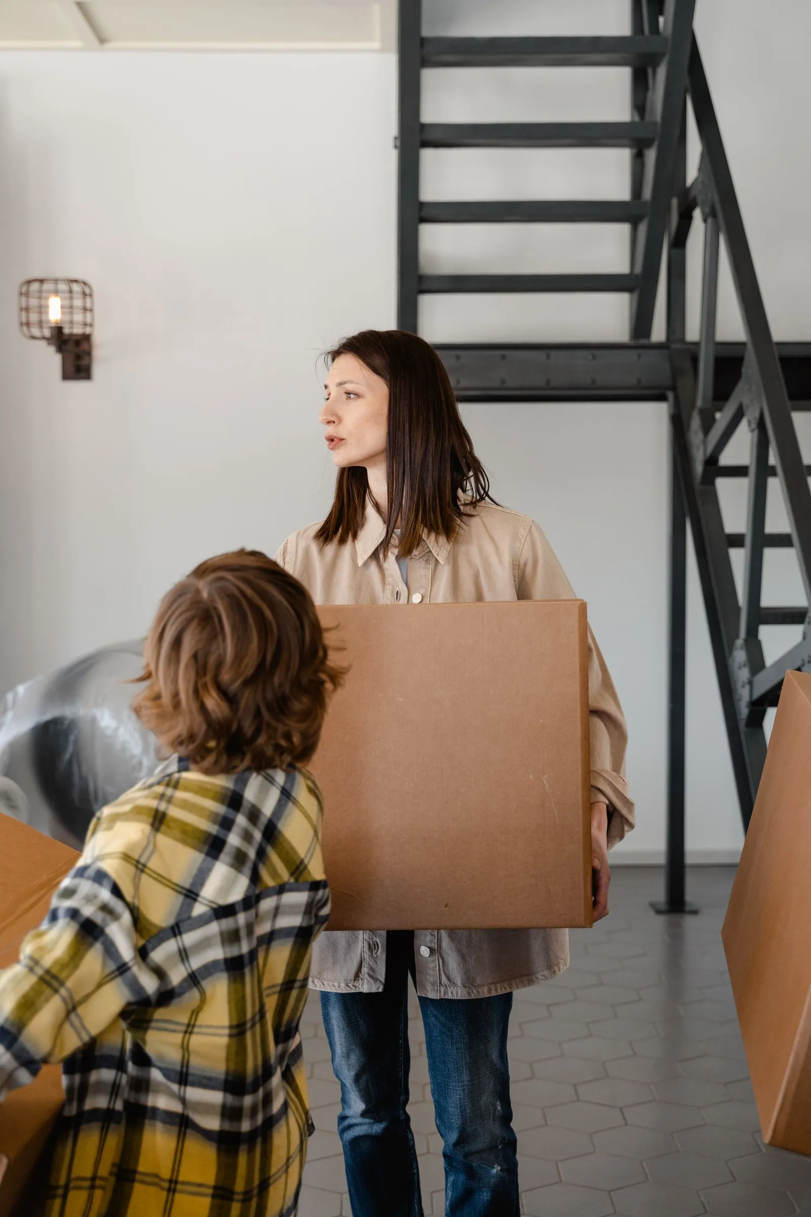 A parent and child carrying boxes into a new home
