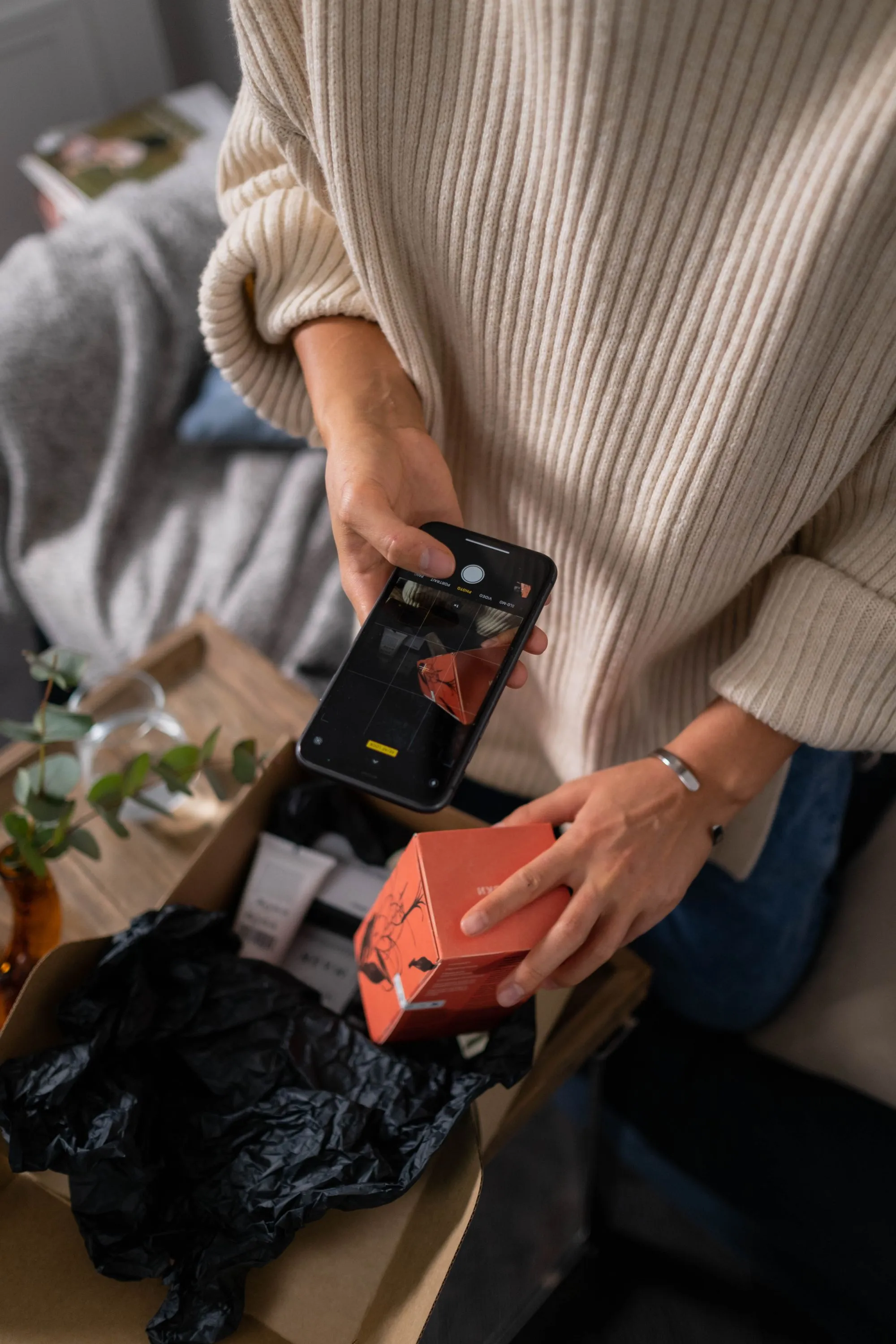 A woman photographing items as she packs them into a box